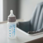 Clear plastic baby bottle on the tray of a high chair.