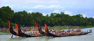 Photo of four snakeboats on a river. Each boat is long and black, with red-orange flags on the stern, and several dozen paddlers.