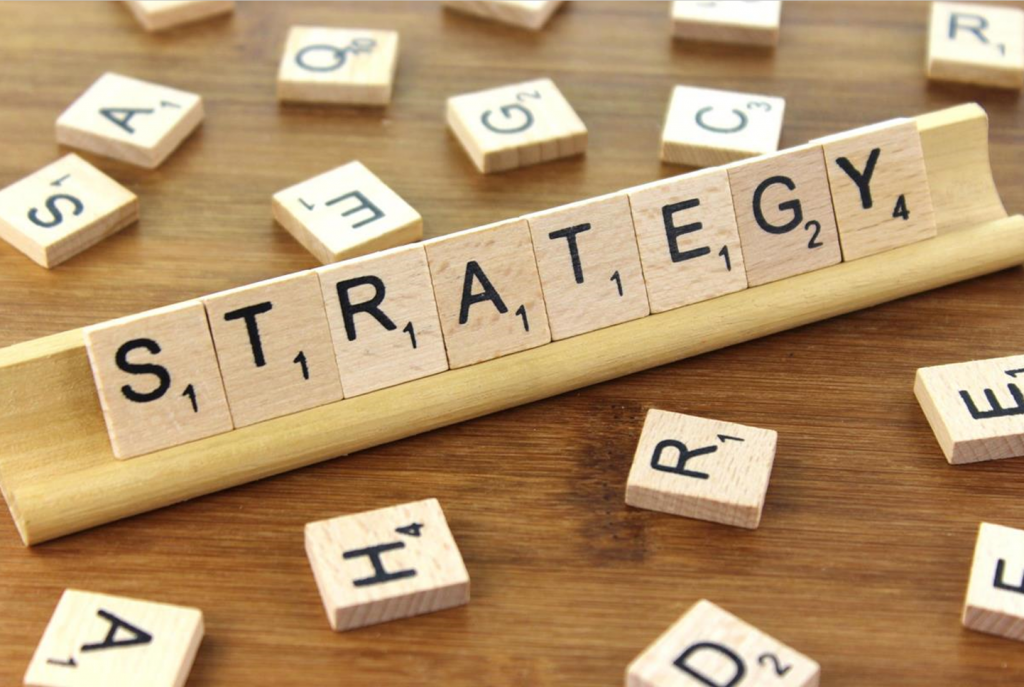 The word strategy spelled out with scrabble tiles on a wooden desk.