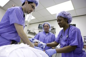 Three students in scrubs practice intubating a volunteer.