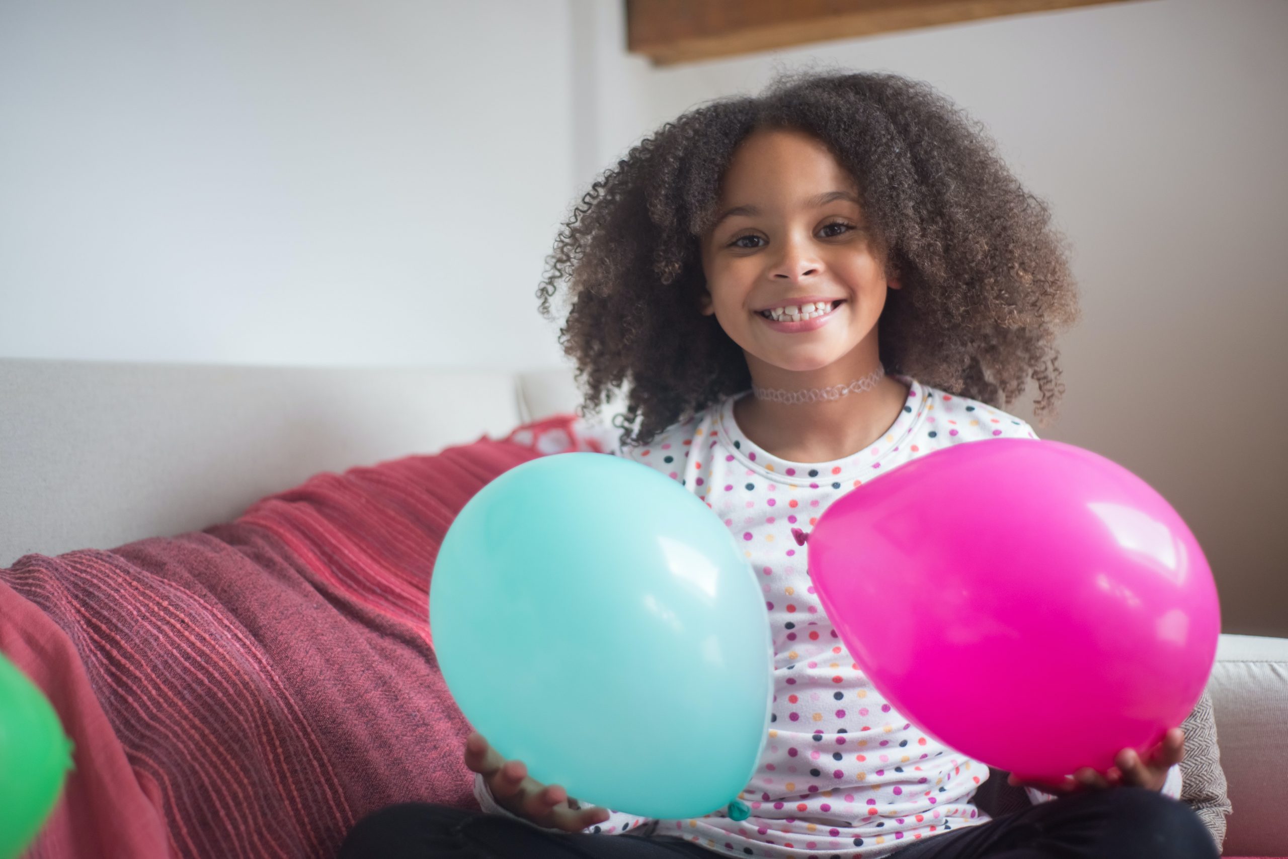 A smiling girl is holding two balloons