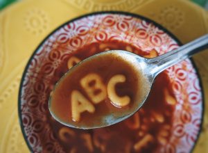 A bowl of alphabet soup. A spoon is raised above the bowl with the letters ABC in it.