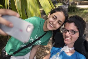 One girl takes a selfie with another girl who has a tracheostomy.