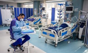 A clinician completed paperwork in the ICU, with ventilated patients in the background.