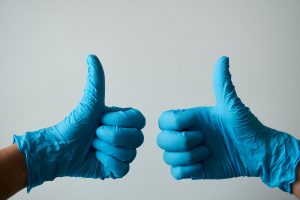 Two blue-gloved hands give a thumbs up.