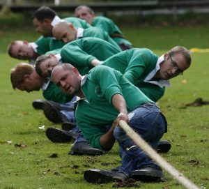 A Tug O War team wearing green shirts braces against the ground and pulls the rope with everything they have.