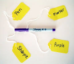 A purple marker lying horizontally with four, yellow tags attached to it. The tags offer different descriptors ~ pen, Sharpie, purple, and marker.