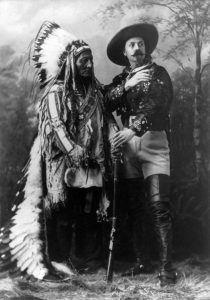 A photograph of Hunkpapa Lakota (Sioux) leader Sitting Bull, and showman William Frederick “Buffalo Bill” Cody standing side by side, each holding the barrel of the rifle placed between them.