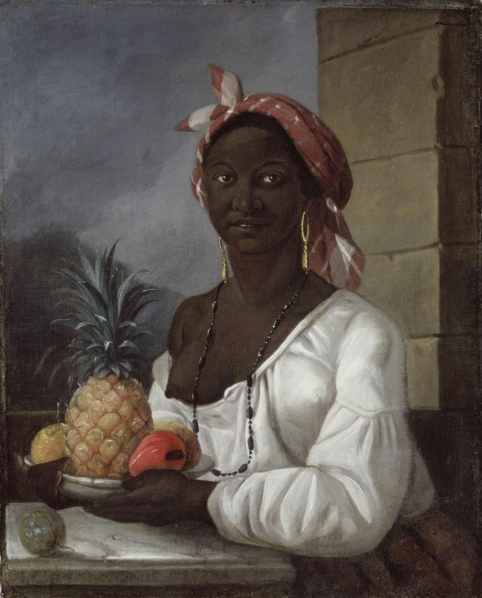 Against a background of stormy gray sky, faint hilltop, and stone wall, a young Black woman seated at a marble-topped table holds a silver bowl of tropical fruit, including a pineapple and a mango. Her loose white shirt’s large neckline droops off her right shoulder, exposing her right breast. She wears a long necklace of black beads, long gold earrings, and a muted red and white patterned headscarf. She looks just beyond the viewer’s right shoulder. We see her figure from the waist up.
