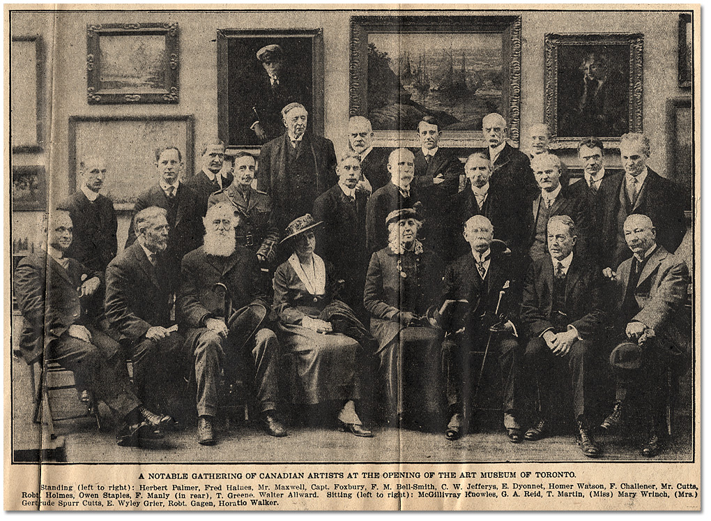 A black and white newspaper photograph from 1918 showing a group of men and two women, posed before an exhibition wall of framed paintings.