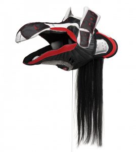 The sculpture strongly resembles an Indigenous Northwest Coast mask in black, white and red, its open mouth pointed left. It is made of deconstructed running shoes and black hair.