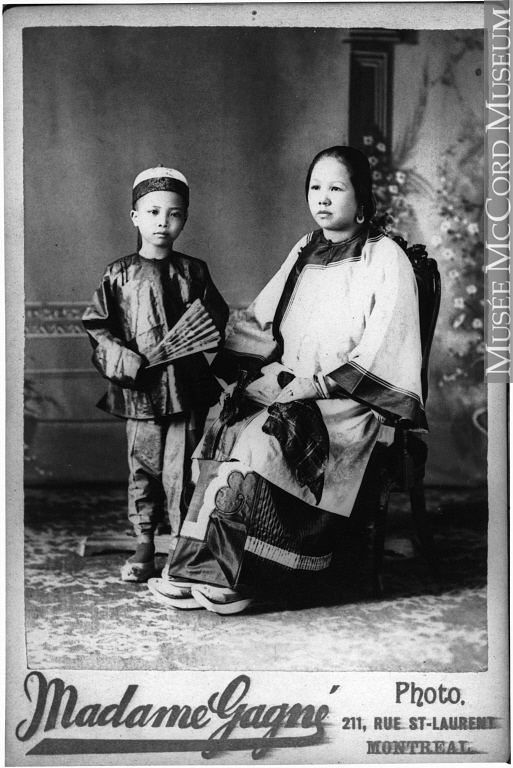 Displayed with a Montreal studio’s stock frame is a black and white photographic portrait of a Chinese woman and a young boy. She sits on an angle, although the boy looks directly at the viewer. They are dressed in traditional tunics and pants.
