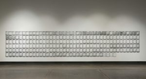 A series of 8 1/2 x 11” pages mounted on a plain white wall, in thirty-five columns and six rows, and a seventh row of 28 pages.