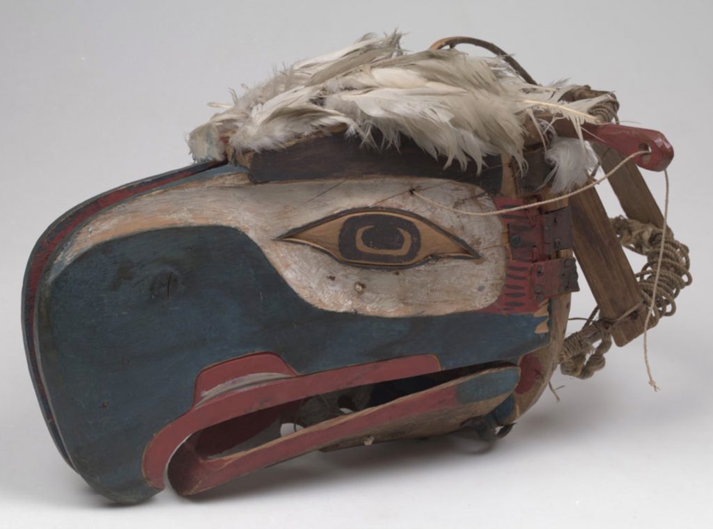 A closed Kwakwaka’wakw transformation mask depicting an eagle’s head made of wood and painted in blue, red, white and black curvilinear lines.