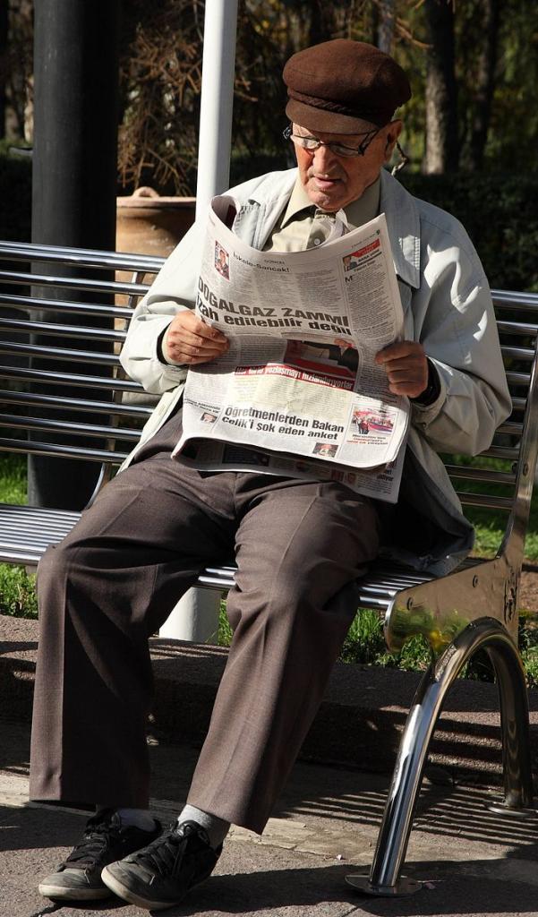 Man reading newspaper on park bench.