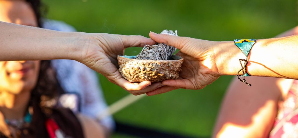 A close-up view on the hands of two spiritual people, passing sacred objects during an outdoor meeting celebrating native culture and tradition.
