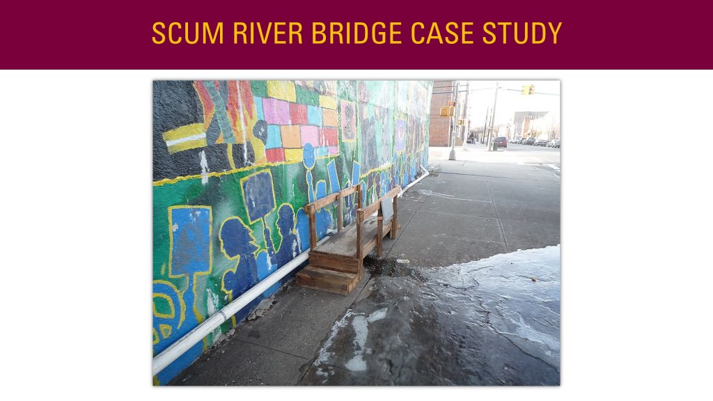 Image of a presentation slide. Title: Scum River Bridge Case Study. Body of slide is a picture of a small wooden bridge that appears handmade. Next to the bridge is a flow of water that appears to originate from a leak.