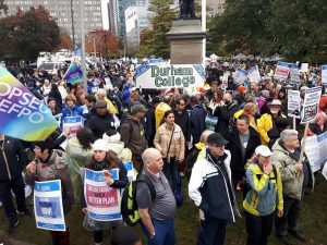 Close up on a group of protester holding banners and sandwich board signs. They are at Queen's Park to show support for striking Ontario faculty.