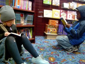 two children reading in front of bookshelves at a bookstore
