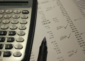 Pen and calculator on a page of numbers with check marks.