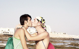 Two men kissing on a beach.
