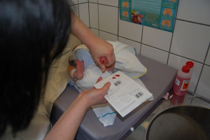 A photo of a doctor taking a blood sample from a newborn, to test for various health conditions including cystic fibrosis.