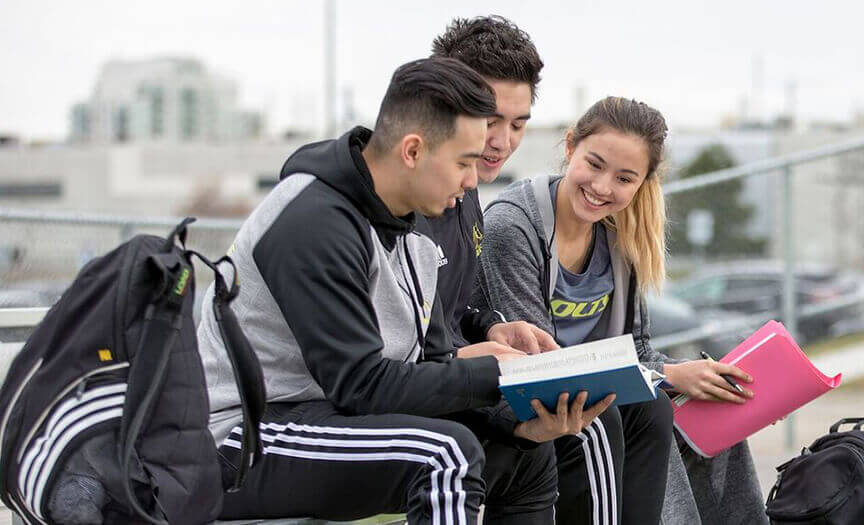 Students sitting outside, taking together, looking at a book