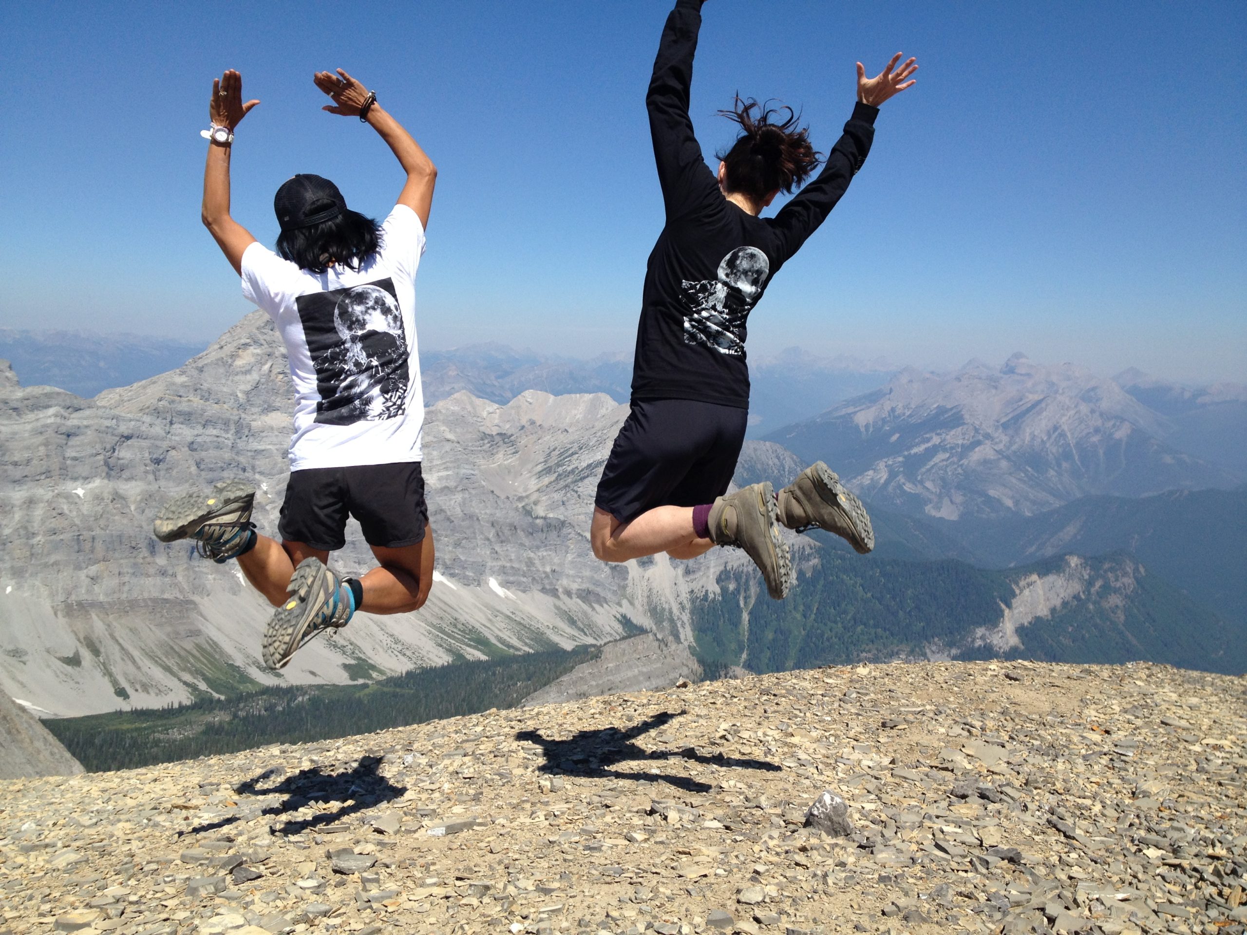 Two people on top of a mountain leaping into the air