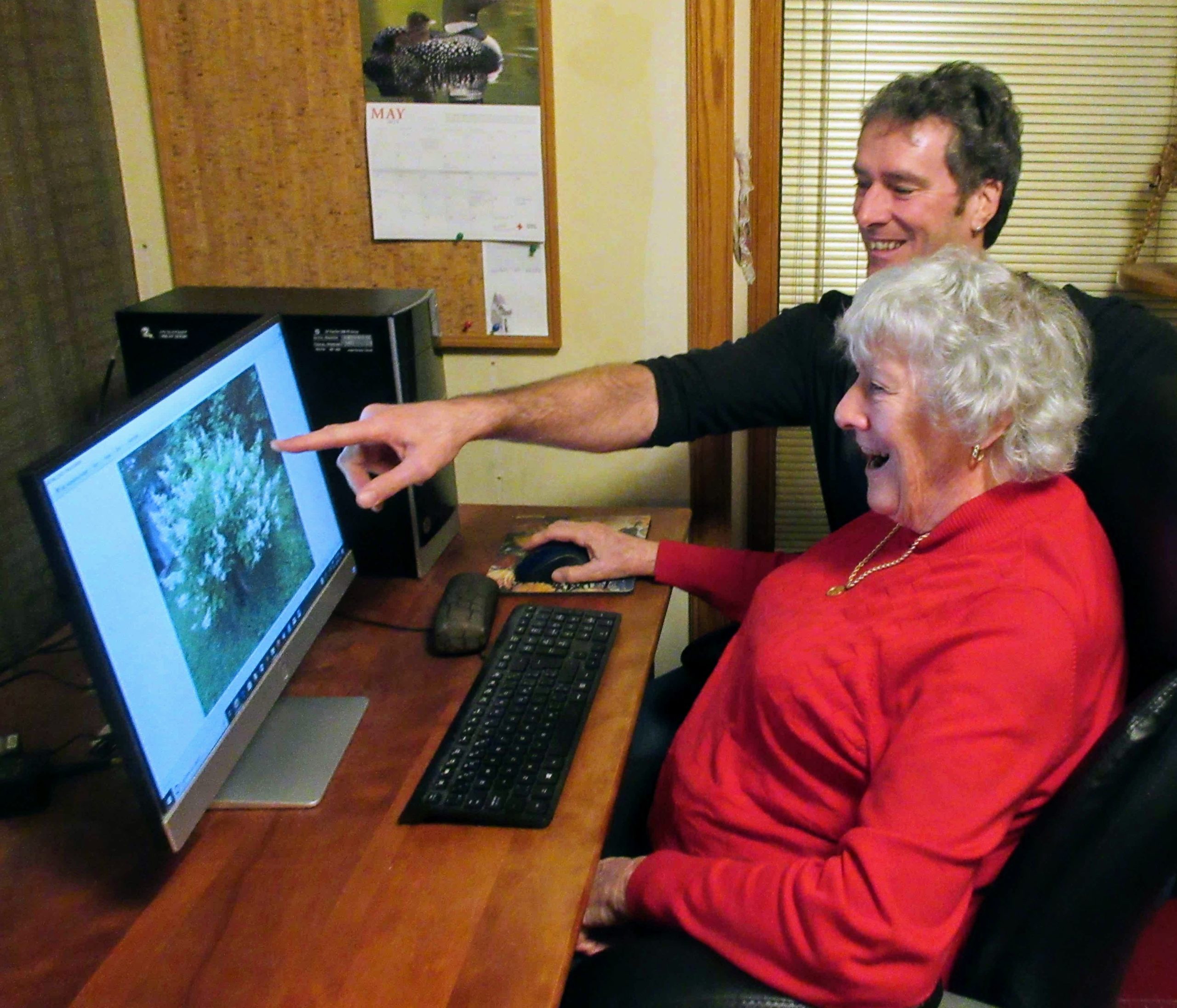 A man teaches an older woman how to use a desktop computer