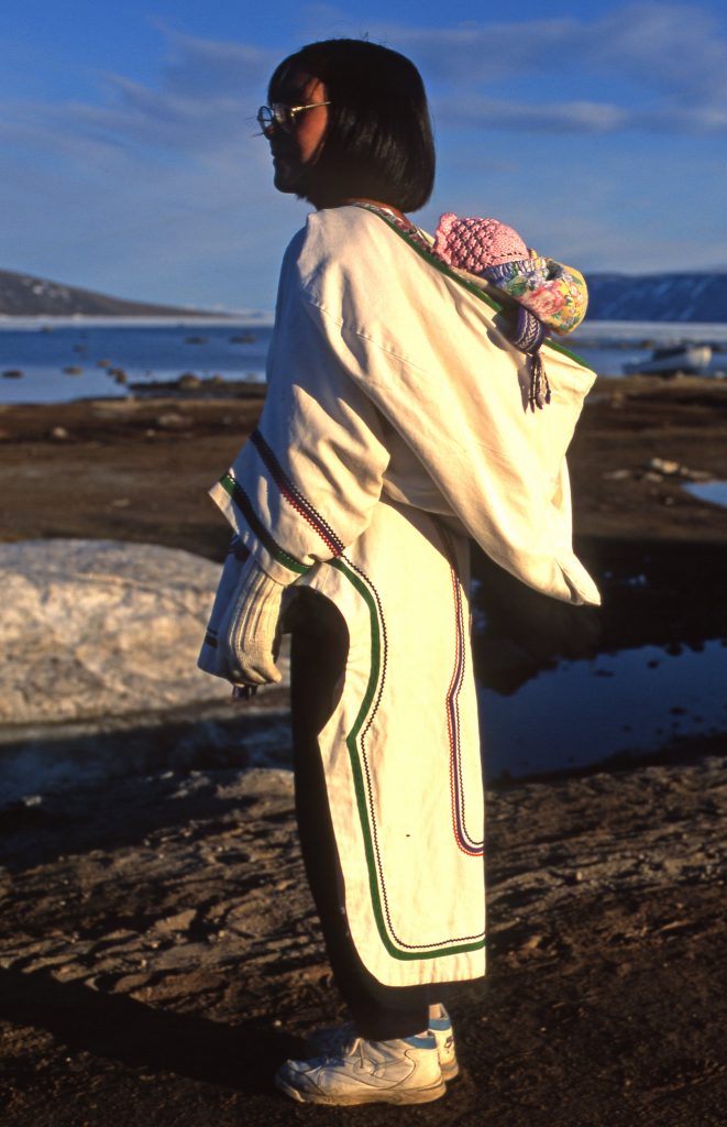 Inuit woman dressed in white and looking to the left, carrying her child on the back in Nunavut Canada