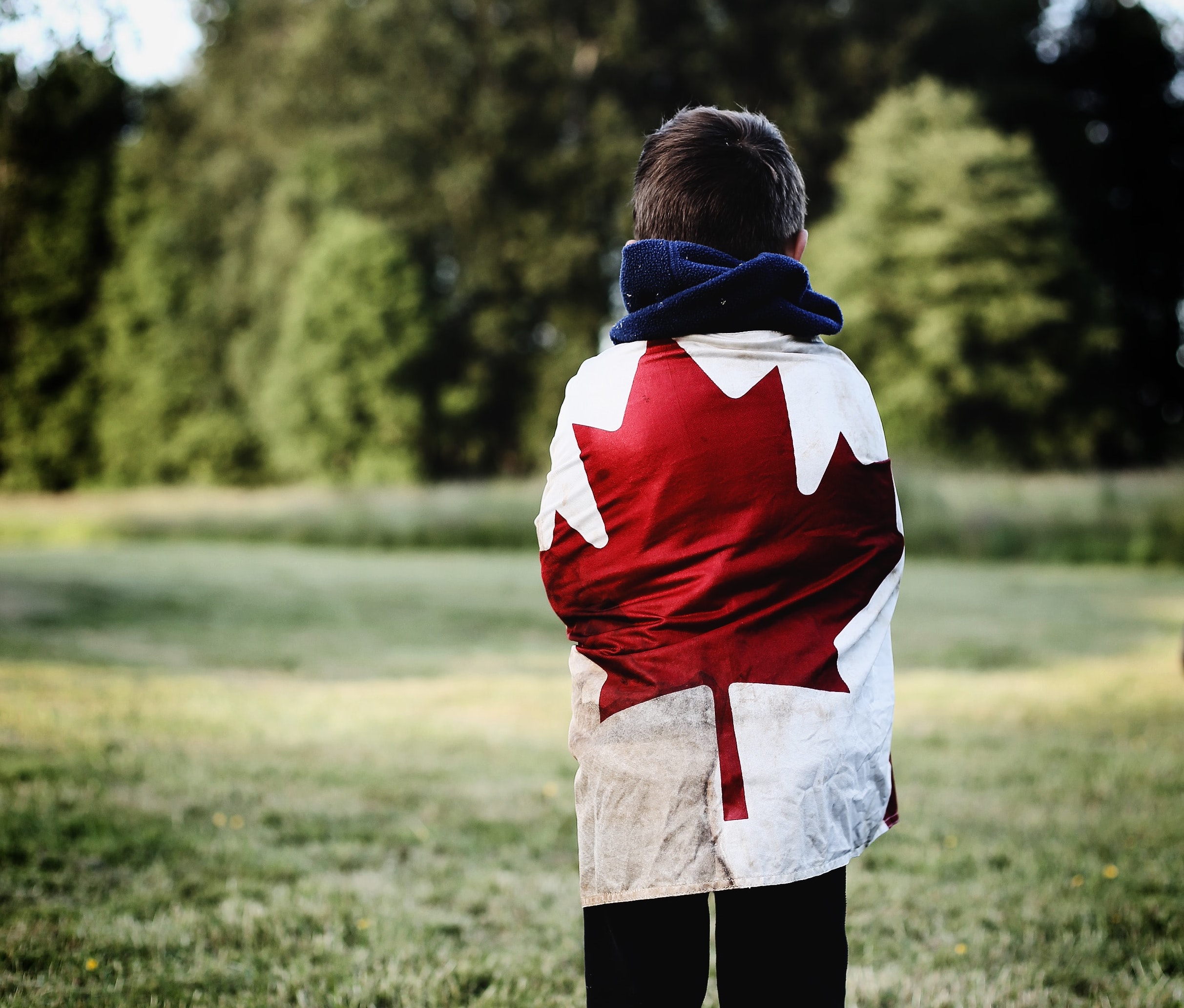 A child wrapped in a Canadian flag overlooks a field.