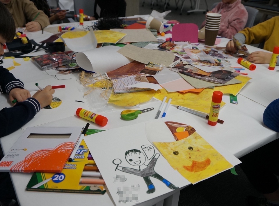 children sitting arount a table covered with craft materials (paper, pens, glue, scissors, etc.)