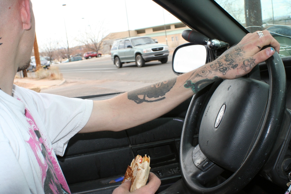 a person sitting in the drivers seat of a car with one hand on the steering wheel and the other holding food