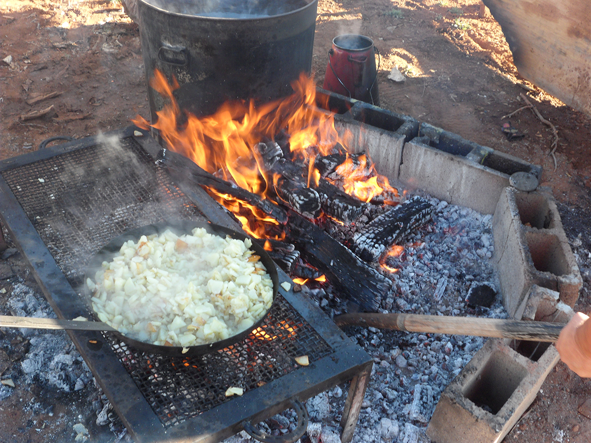 a panful of food sitting on a grill over an outdoor fire