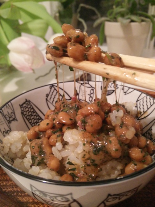 imagea bowl of rice with chopsticks holding a cluster of seasoned natto beans