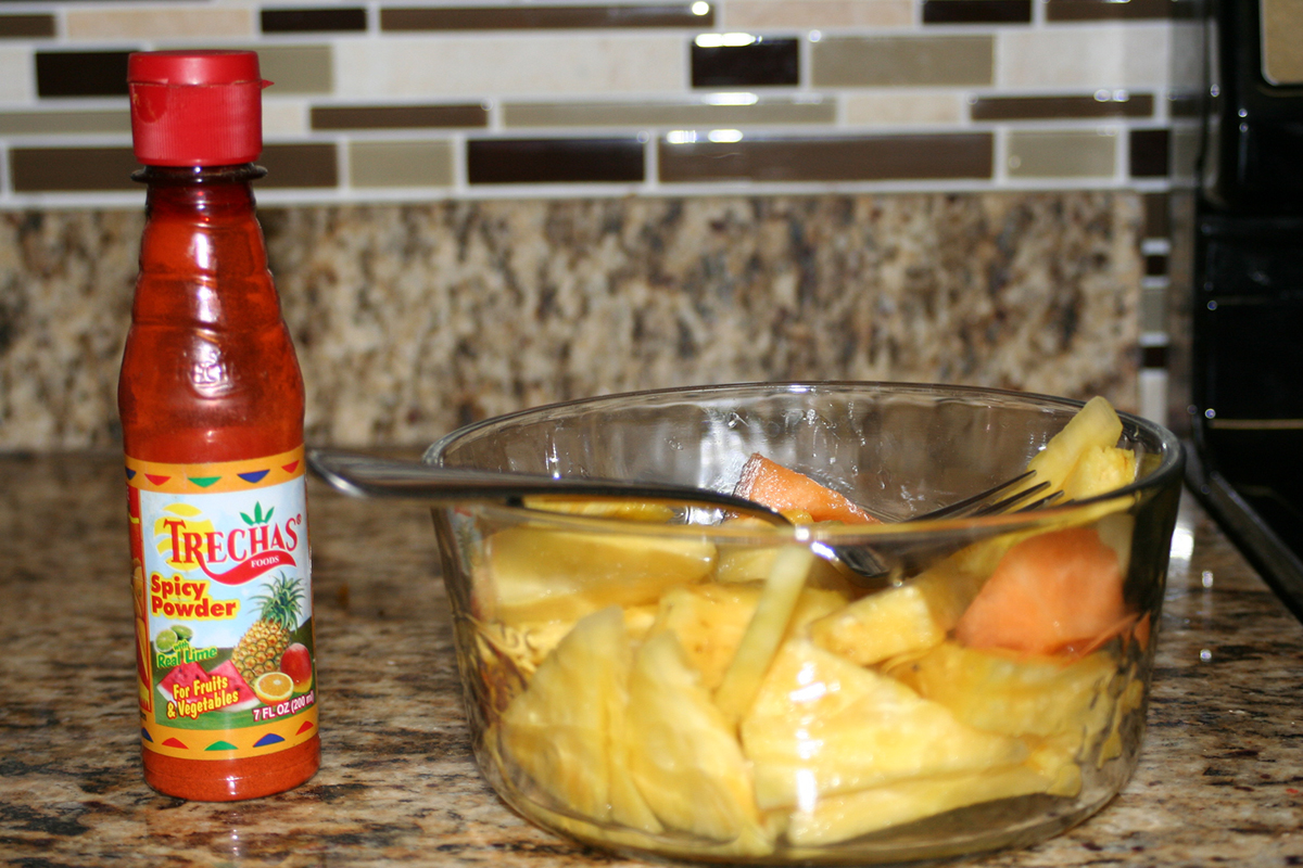 a bowlful of pineapple pieces witha bottle of Trechas Spicy Powder seasoning