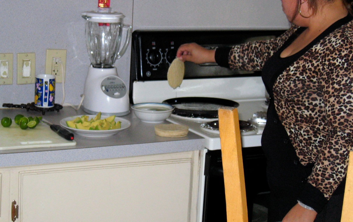 a person in a kitchen holding a tortilla above a panful of oil