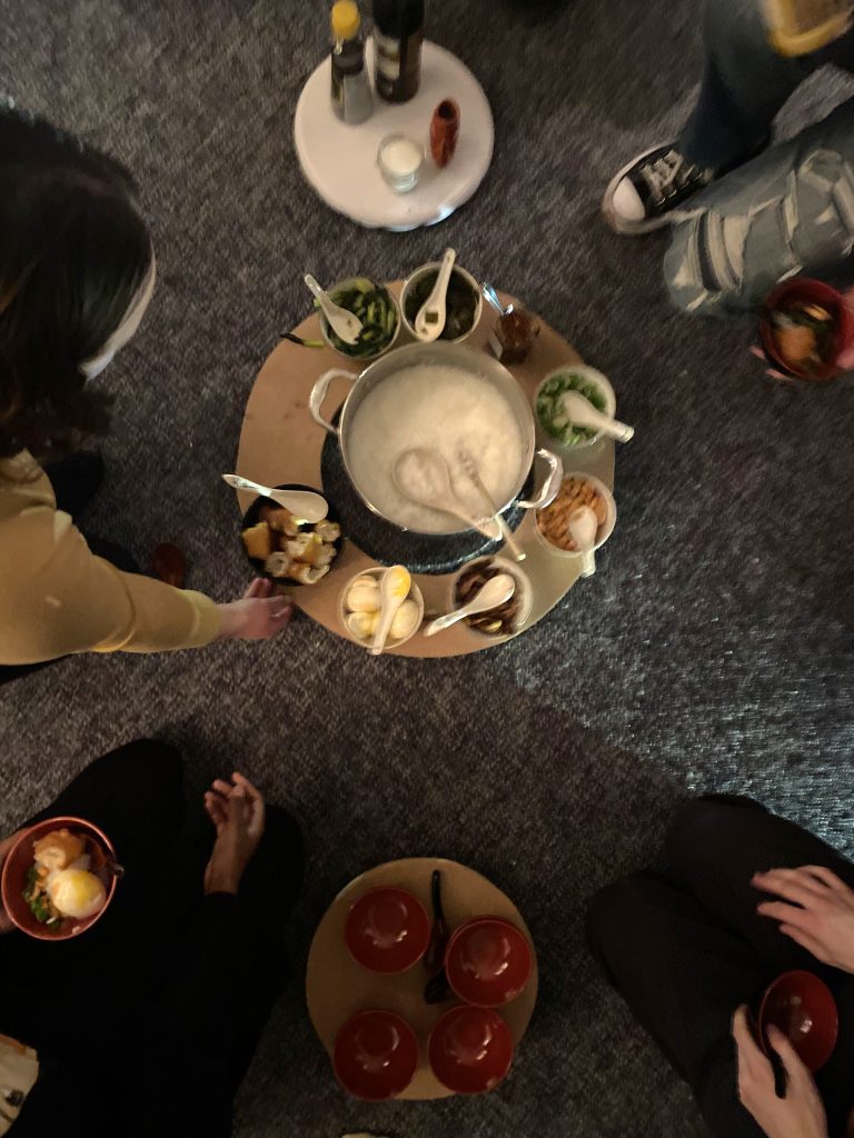 people assembling around bowls of congee and ingredients sitting on the floor