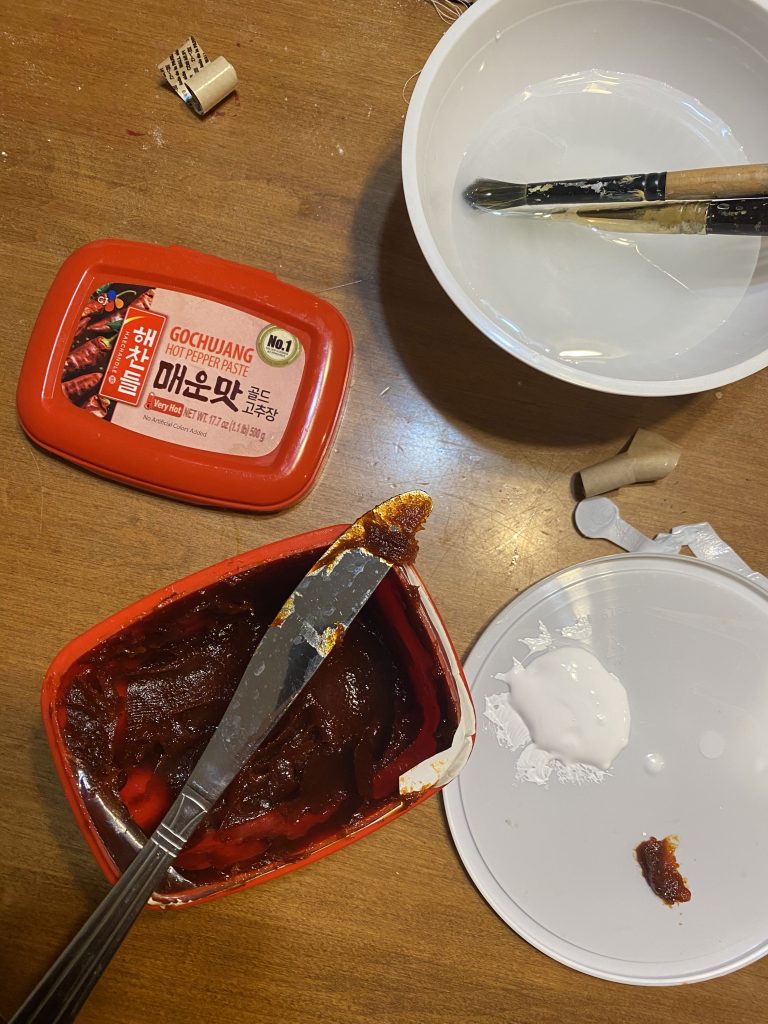 an open container of gochujang (red chile paste) and artist's gesso with knife and paintbrush