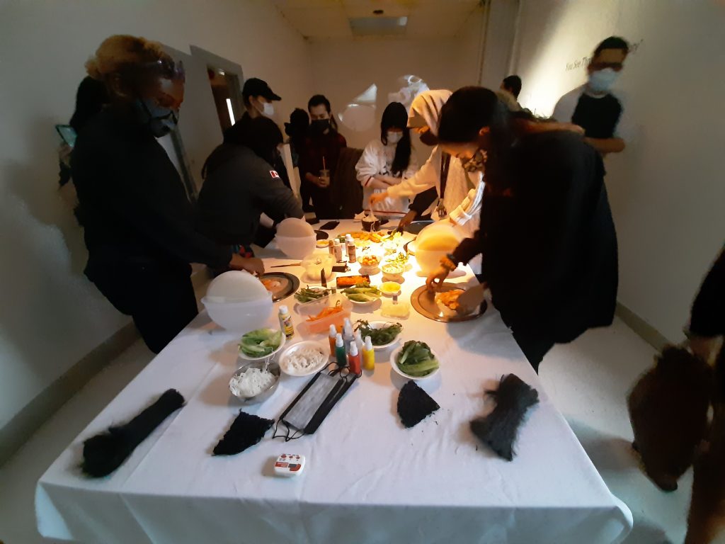 people gathered around a table of food in a gallery space
