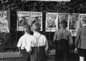 Four young boys read propaganda .posters titled 'Die Woche.'
