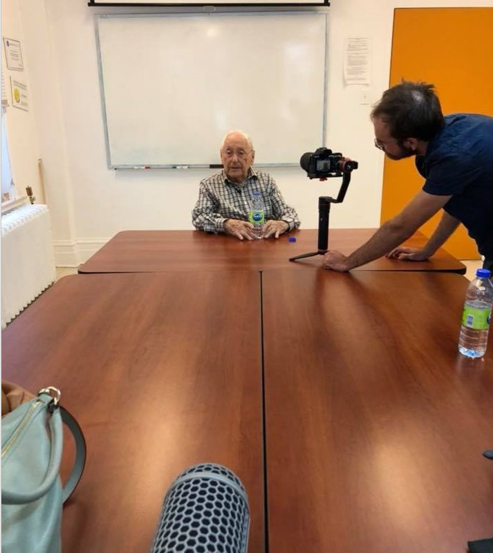 Ted Bolgar sitting at end of a long table with a camera and microphone in view.