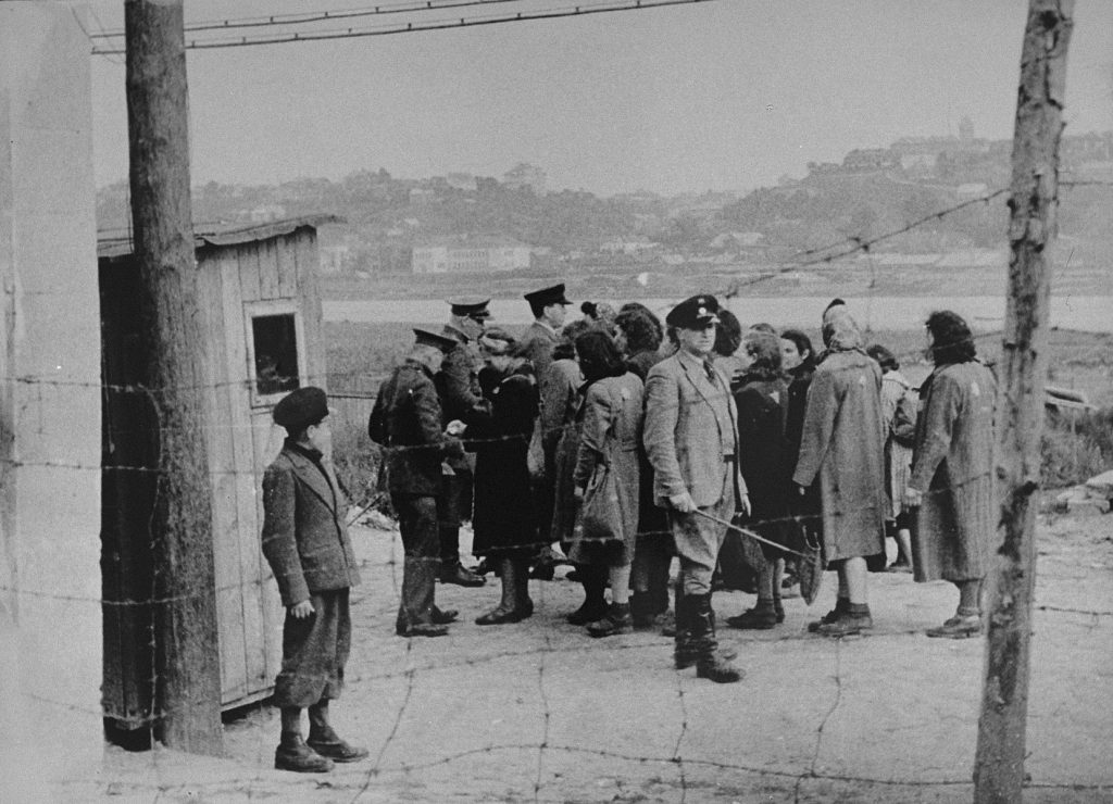 A group of Jewish women are lined-up to be searched by German and Lithuanian guards.