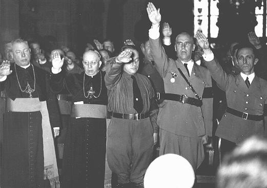 Le clergé catholique et les responsables nazis, dont Joseph Goebbels (à l'extrême droite) et Wilhelm Frick (deuxième à partir de la droite), font le salut nazi.