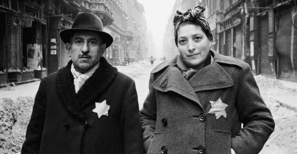 A Jewish couple wearing stars walking in the streets.