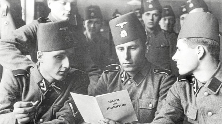 Cette photo montre trois soldats assis à une table en train de lire une brochure intitulée « Islam et Judaïsme »