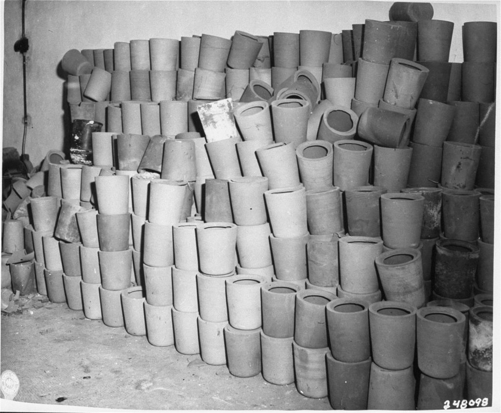 Des urnes en argile sont empilées sur huit à neuf rangées dans une salle en ciment sous le crématoire de Dachau.