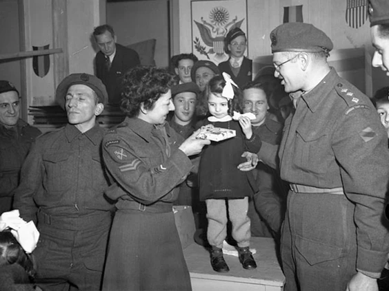 Corporal M. Freeman, Canadian Women’s Army Corps (C.W.A.C.), and H/Captain Samuel Cass, Jewish chaplain, presenting a gift to a Belgian girl during a Hanukkah celebration, Tilberg, Netherlands, 17 December 1944.