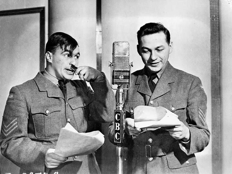 Wayne and Shuster dressed in military uniforms reading from a script and speaking into a CBC microphone.