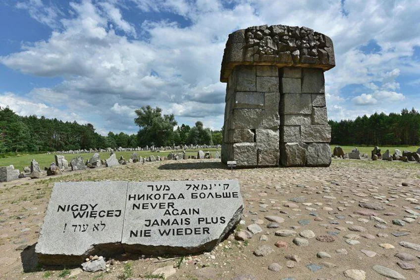The multilingual plaque in the foreground of the memorial reads ‘Never Again’.